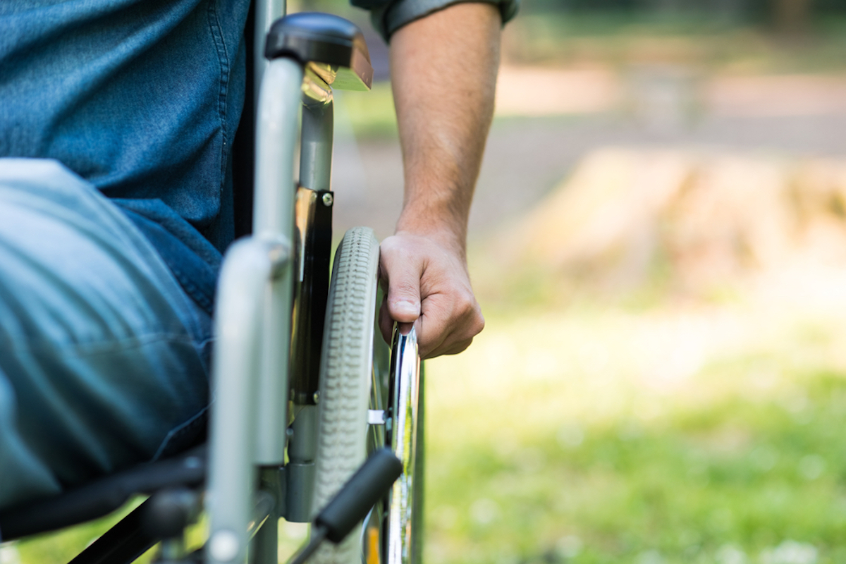 Detail of a man with a wheelchair in a park.