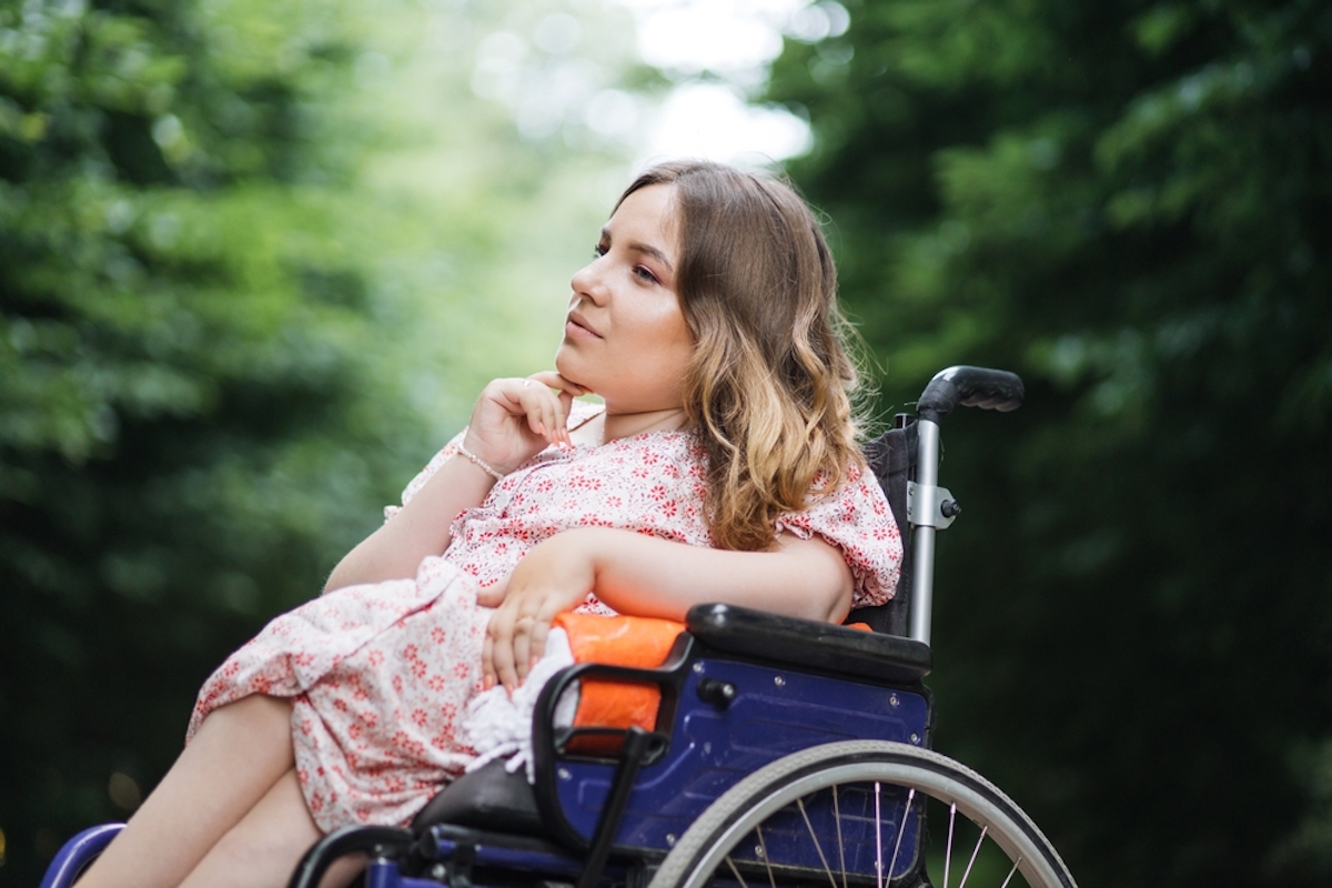 Female Person with Spinal Muscular Atrophy Spending Time Outdoors Alone with Her Thoughts Young Woman Who Using Wheelchair Sitting Among Green Summer Park and Looking Aside