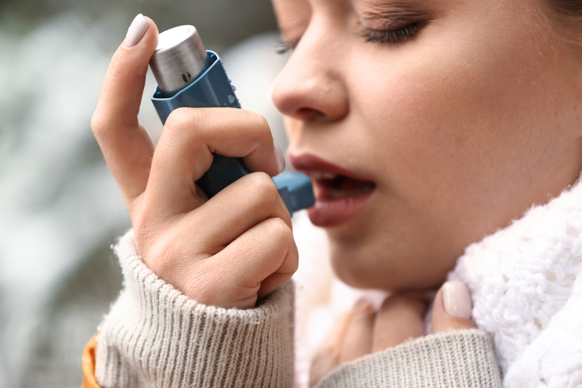Young woman with inhaler having asthma attack outdoors, close-up 