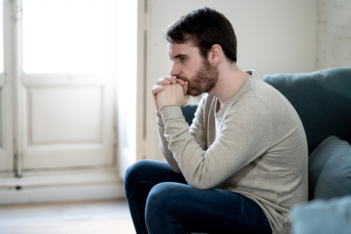 Unhappy depressed white man sitting and lying in couch in living room feeling desperately lonely and suffering from depression. In stressed from work, anxiety, deeply sad and men Health care concept.