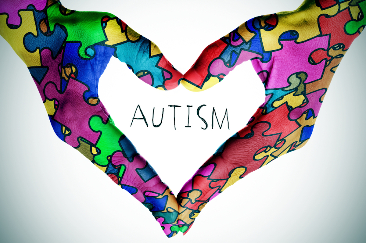 woman's hands forming a heart pattern with many puzzle pieces of different colors, symbol of autism spectrum disorder awareness, and the text autism, with a light vignette added