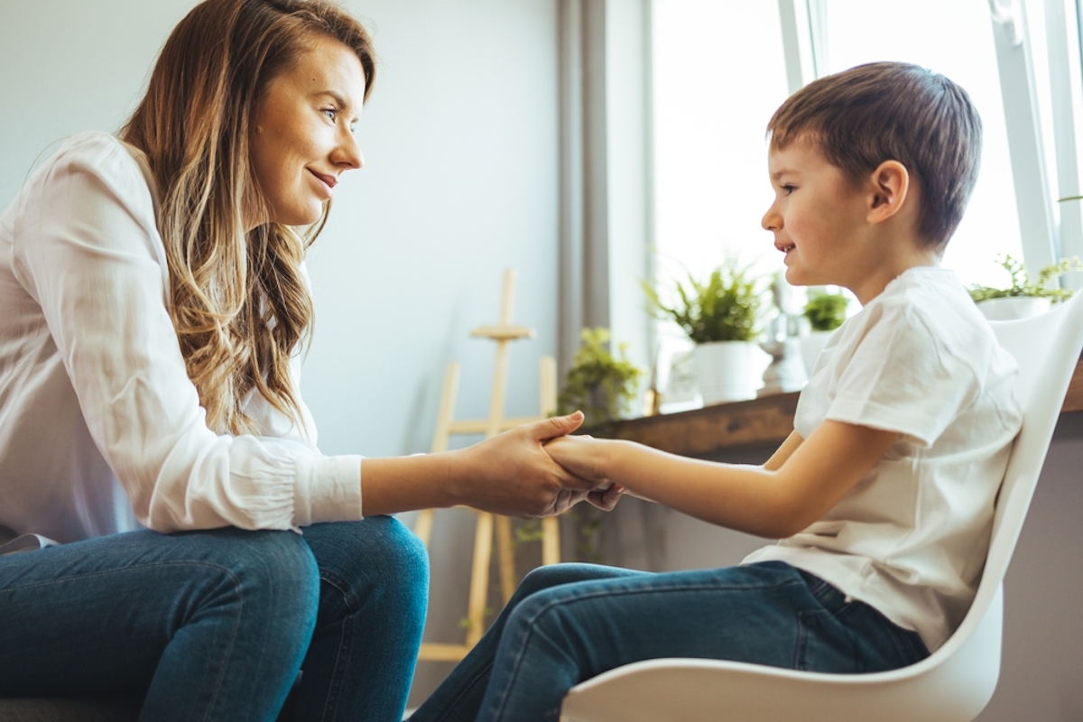 Young boy having therapy with a child psychologist. Smiling woman talking to boy. Friendly young child psychologist talking with little boy suffering from emotional disorder in bright office 