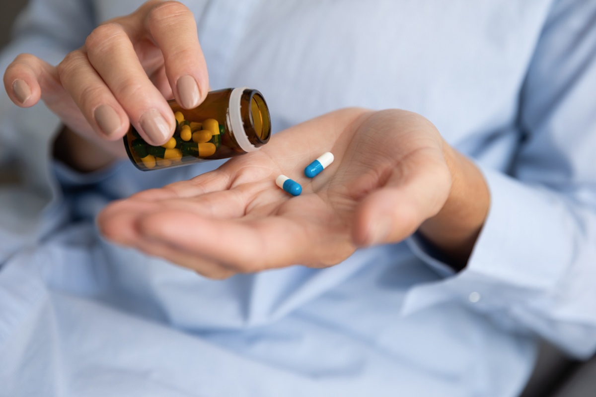 Oudere zieke zieke vrouw houdt twee pillen bij de hand gieten capsules uit medicijnfles neem pijnstillers supplement medicijn, oude senioren farmaceutische gezondheidszorg behandelingsconcept, close-up view