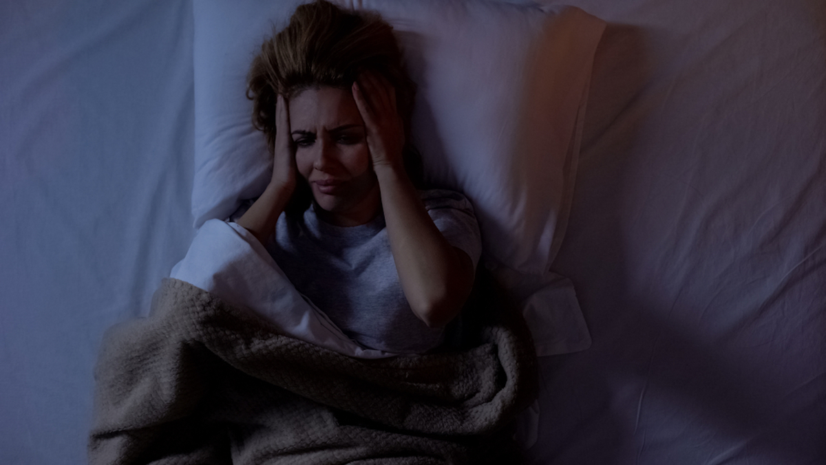 Woman having terrible headache lying in bed at night, strong migraine, top-view 