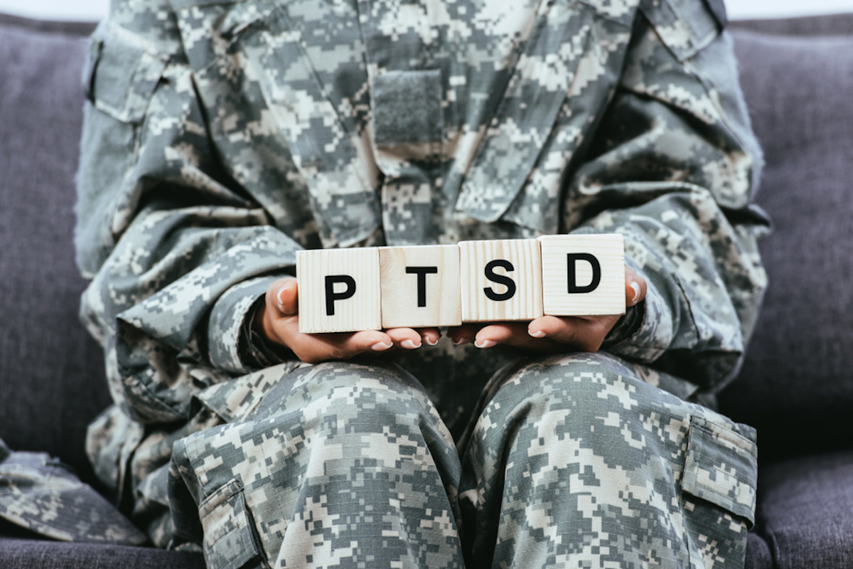 cropped shot of female soldier in military uniform sitting on bench and holding wooden cubes with PTSD sign