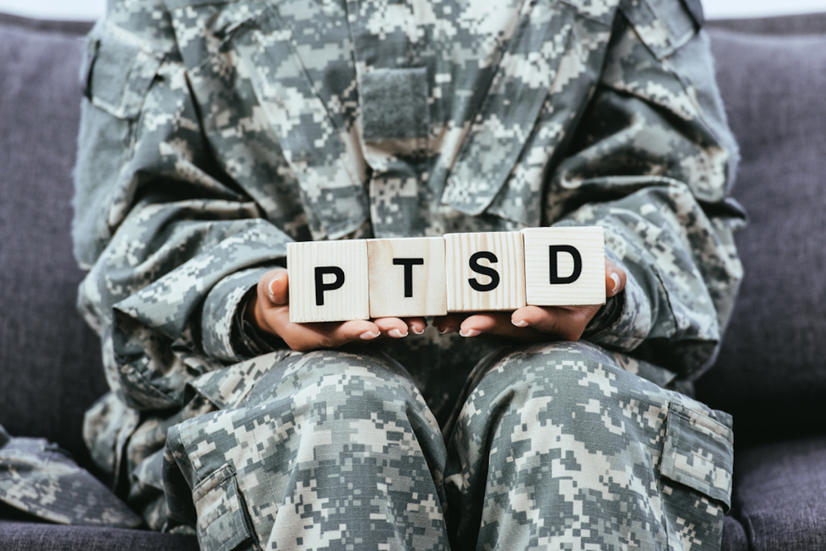 Cropped Shot of Female Soldier in Military Uniform Sitting on Bench and Holding Wooden Cubes with Ptsd Sign