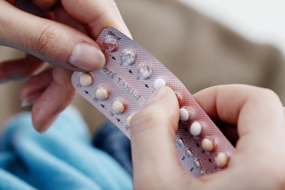 Zoomed in picture of a Caucasian woman pushing a birth control pill out of the strip.