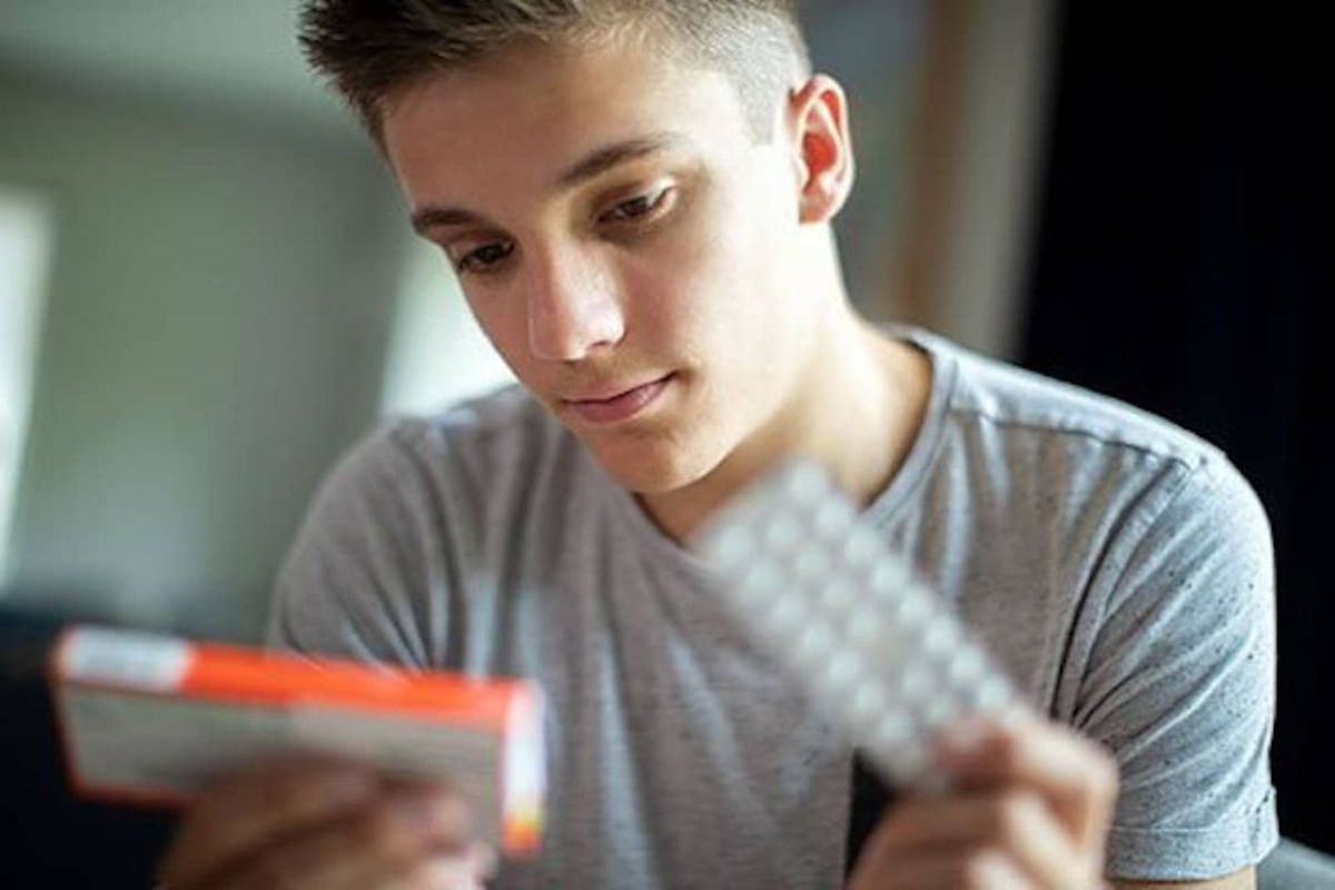 Young Caucasian male looking at a medicine box in one hand. In his other hand he is holding a medicine strip